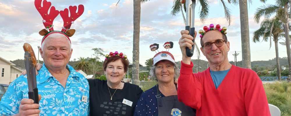 Men and women with xmas hats and holding up sausages with tongs
