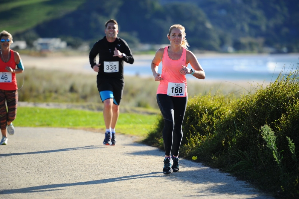 two women running in pink and man running in black on coastal path