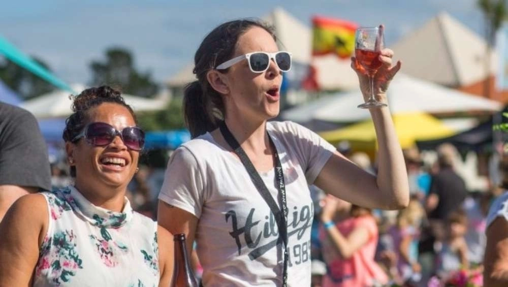 Two women smiling and standing at festival with wine glass in hand