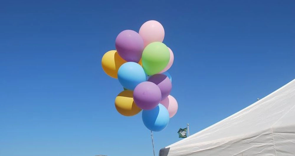 Bunch of coloured balloons tied to white tent on blue sky
