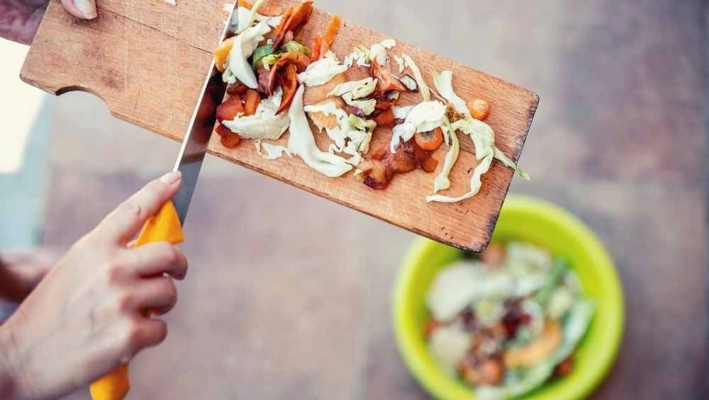 Organic waste being pushed off chopping board into bucket
