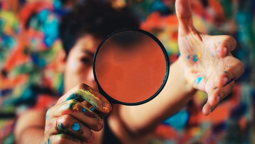 Person holding magnifying glass with paint cover hands