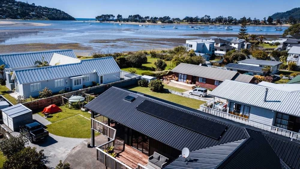 aerial looking over house roof with solar panels and out to water with boats moored